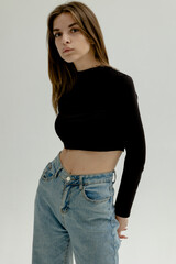 a woman posing on a light background dressed in jeans and a black top