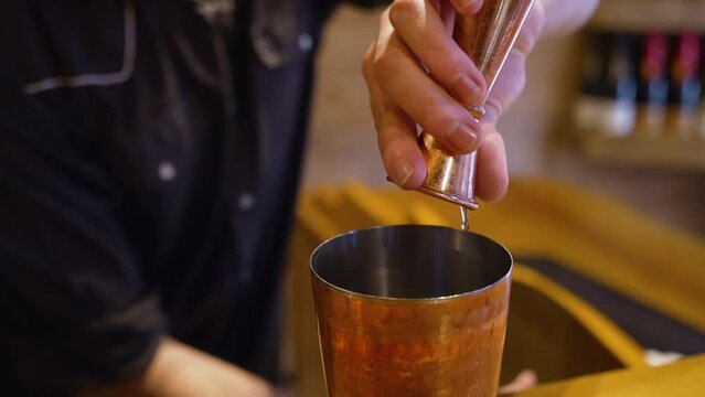 Bartender pours brown liquor shot into copper shaker, measuring jigger, slow motion close up 4K