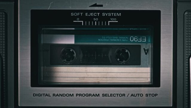 Audio cassette rotates in deck of old tape recorder. Audiocassette with blank label in retro player spinning and playing. Close-up. Retro call recording, playback, reel playing, vintage technology