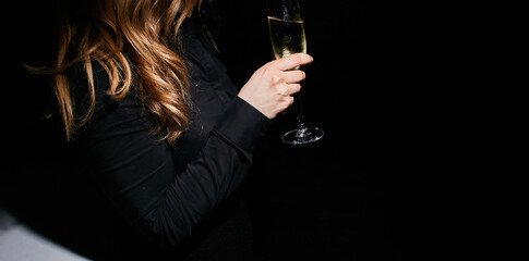 girl holding a glass of champagne in her hand on a black background.