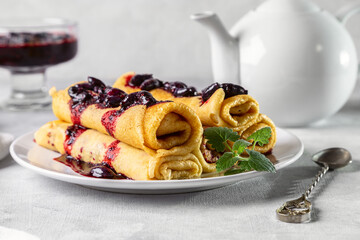 Rolled pancakes with honeysuckle jam on a plate with a mint leaf