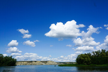 Bright blue sky with white clouds, river, trees and mountains