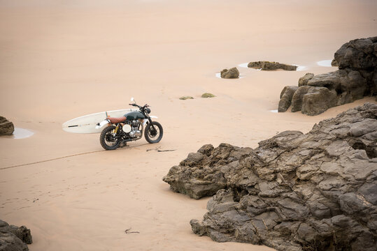 Motorcycle and surfboard parked on sandy beach