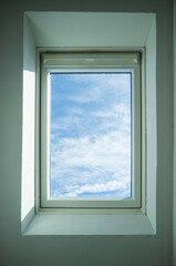 Closed roof window through which you can see the blue sky and white clouds on a sunny day. Bottom view.