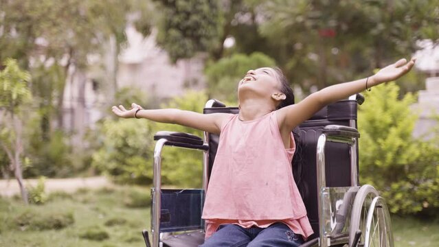 concept of freedom, individuality and courage showig by Happy girl kid feeling nature by stretching arms while sitting on wheelchair at hospital park.