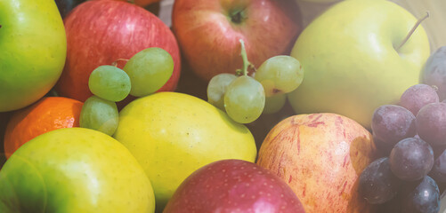 Ripe juicy fruit, like apples, and grapes in a pile, lit by soft morning sunshine. Selective focus.
