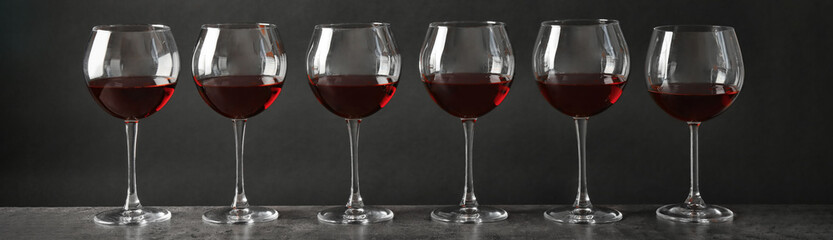 Glasses with tasty red wine on grey table. Banner design