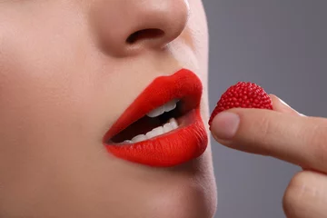 Fotobehang Young woman with beautiful red lips makeup eating candy on grey background, closeup © New Africa
