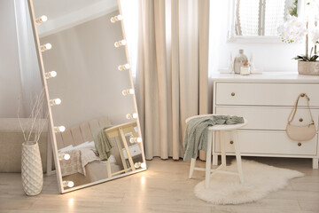 Large mirror with light bulbs and chest of drawers in stylish room. Interior design