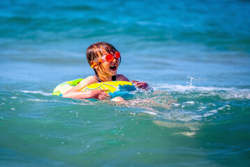 Happy child girl swimming on the waves of sea. Summer vacation and healthy lifestyle concept.