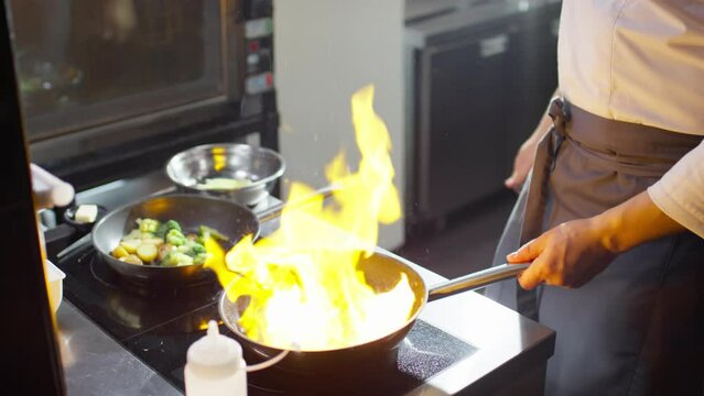 Cropped shot of chef making fire in frying pan with lighter and flambeing fish in restaurant kitchen