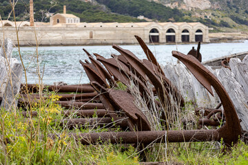 Old anchors on the port of Favignana with the Florio factory in the background. Favignana, (Egadi) Aegadian Islands, Trapani, Sicily, Italy © Giuma