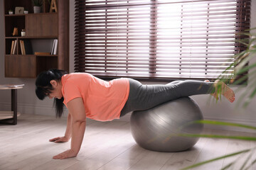 Overweight mature woman doing exercise with fitness ball at home