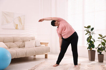 Overweight mature woman stretching at home, space for text