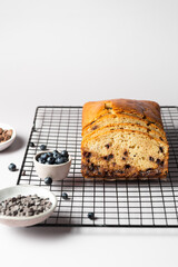 Vanilla cake with chocolate drops and blueberries on a culinary lattice, with ingredients on a light gray background with copy space