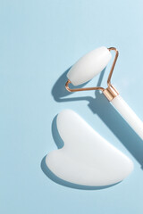 Fototapeta White jade roller and gua sha tool on pastel blue background. Trendy beauty tool. Minimal composition. obraz