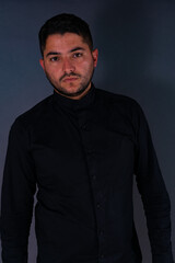 A man in a black shirt, posing on a gray background looking at the camera. Emotions, joy and fun of men.