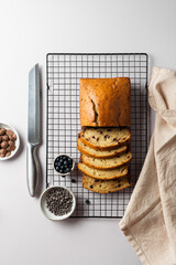 Top view vanilla cake with chocolate chip on a culinary lattice, with bowl of milk and dark chocolate drops and blueberry on a light gray background