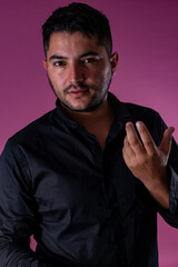 A man in a black shirt, posing on a pink background looking at the camera with a surprised gesture. Emotions, joy and fun of men.