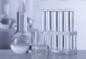 Different laboratory glassware with transparent liquid on wooden table against blurred background