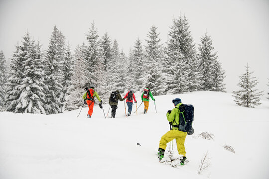 Male skier in green and yellow ski suit with backpack taking photo of group of skiers