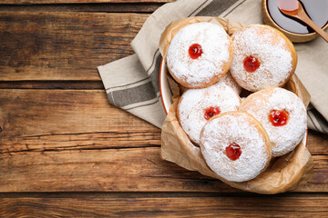 Delicious donuts with jelly and powdered sugar in baking dish on wooden table, flat lay. Space for text