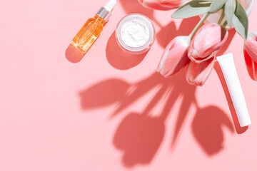 Spring cosmetic flat lay frame with flowers on pink, copy space, top view.