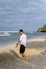 Young handsome man with a charming smile in sunglasses on the beach.
