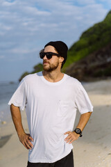 Young handsome man with a charming smile in sunglasses on the beach.