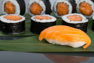 close-up, on a dark table with a reflection, on a bamboo leaf, sushi and Japanese rolls with salmon