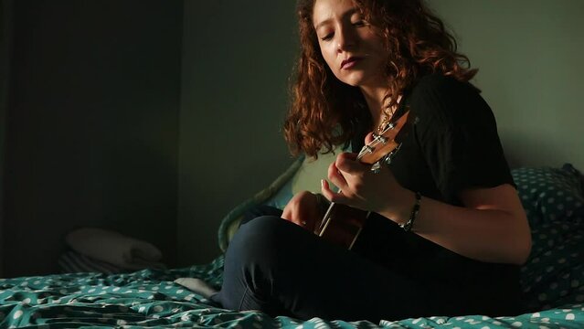 Mujer tocando el ukulele y cantando en su habitaci&oacute;n. Concepto de musica.