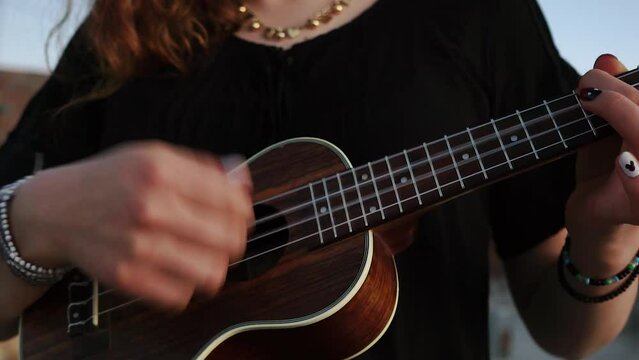 Detalle de manos tocando un ukulele en habitaci&oacute;n.