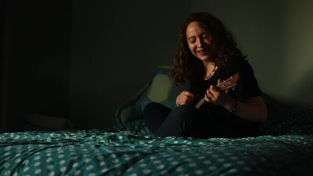 Mujer tocando el ukulele y cantando en su habitaci&oacute;n. Concepto de musica.