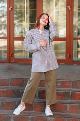 The girl is a model showing fashionable outerwear on the street, on the veranda of a summer cafe. Clothes for the showroom