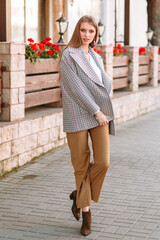 The girl is a model showing fashionable clothes on the street. Behind the girl is a cafe fence