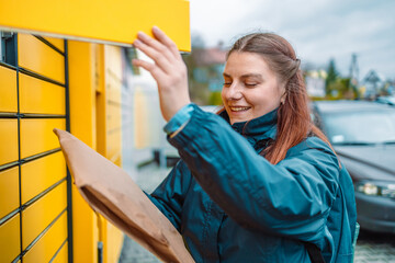 Caucasian woman send or receive parcel with yellow self service post terminal machine. 