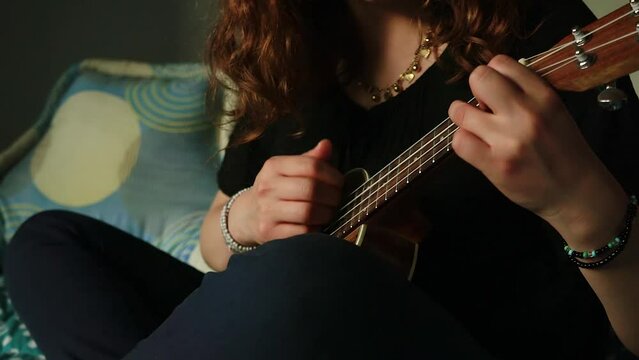 Detalle de manos tocando un ukulele en habitaci&oacute;n.