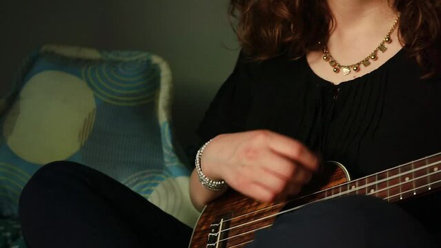 Detalle de manos tocando un ukulele en habitaci&oacute;n.