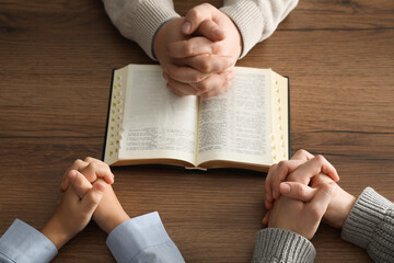 Boy and his godparents praying together at wooden table, closeup
