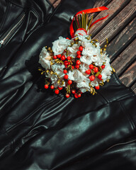 wedding decor. informal wedding bouquet white flowers with red berries on the black leather jacket background at sunny day. wedding concept, free space