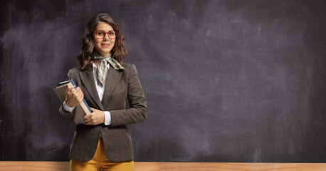 Female teacher holding books and posing in front of a chalkboard