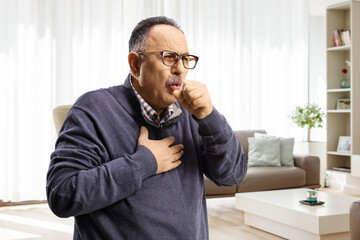 Mature man at home in a living room caughing and holding his chest