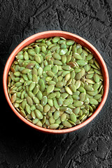 Peeled pumpkin seeds in a bowl on a black background. Super food. Healthy food. Copy space. Flat lay. Vertical orientation