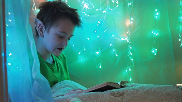 a teenager with long ears reads a book sitting on a bed decorated with garlands. wrapped in a blanket. elf costume