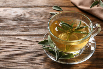 Cup of aromatic sage tea and fresh leaves on wooden table. Space for text