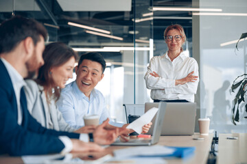 Fototapeta premium Smiling confident businesswoman wearing eyeglasses on business meeting with colleagues in office 