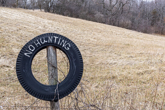 A homemade No Hunting sign painted in white on a tire in front of a farm field in the fall.