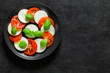 Caprese, Italian antipasto, tomato, mozzarella and basil appetizer, on dark background, top view, space to copy text..