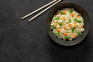 Instant noodles, cooked with vegetables, in a gray bowl and chopsticks, on dark background, top view, space to copy text.
