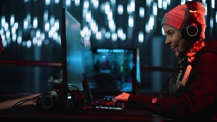 Excited smiling teenager in a gaming tournament plays a game sitting at a computer in an arena with light effects.